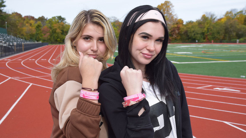Two students showing their pink wristbands.