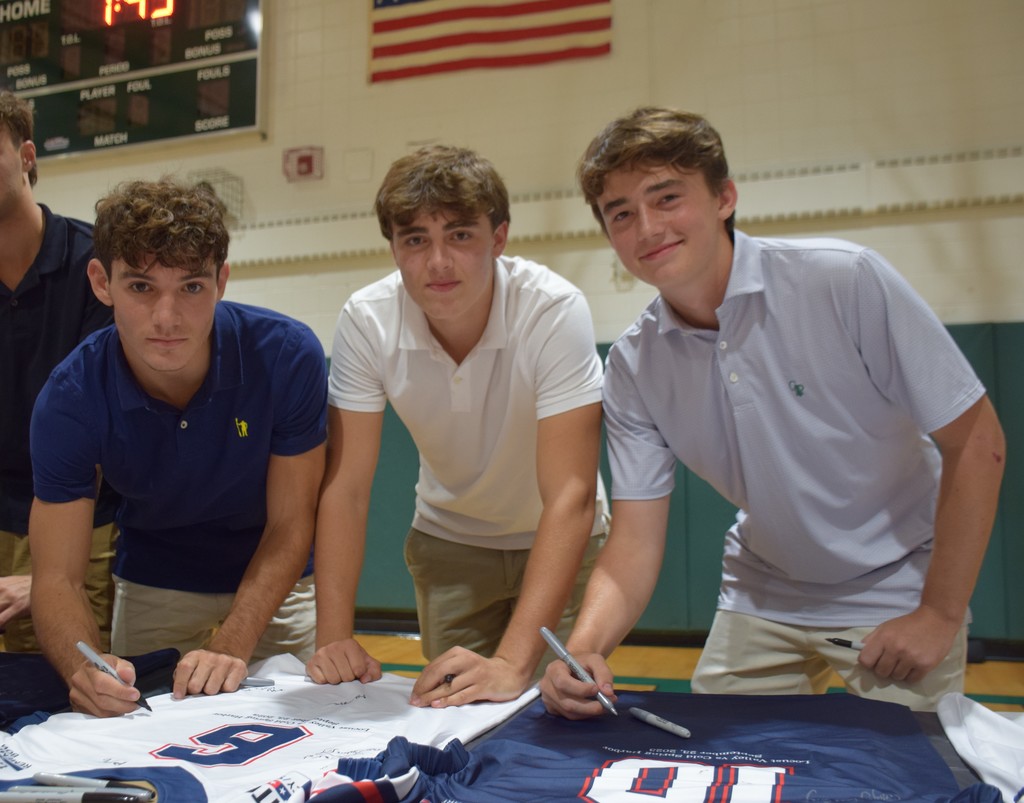 Locust Valley High School varsity football players Michael DiLorenzo, Eric Watts and Phil Terrell sign jerseys that they wore in the Remembrance Bowl at a ceremony on Sept. 21.